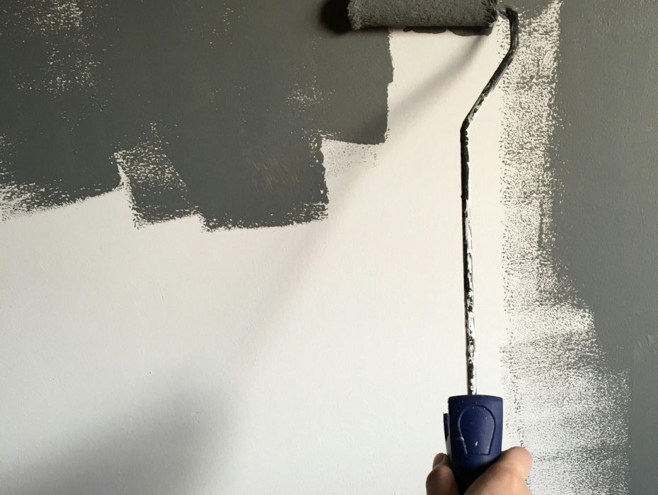 Persona pintando una pared blanca con pintura gris oscuro usando un rodillo manual de pintura