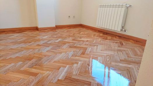 Parquet de madera en espiga con acabado brillante, habitación con zócalo de madera y radiador de pared