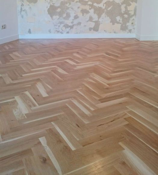 Suelo de parquet de pino melis restaurado en espiga, acabado natural mate, pared con restos de pintura en proceso de renovación