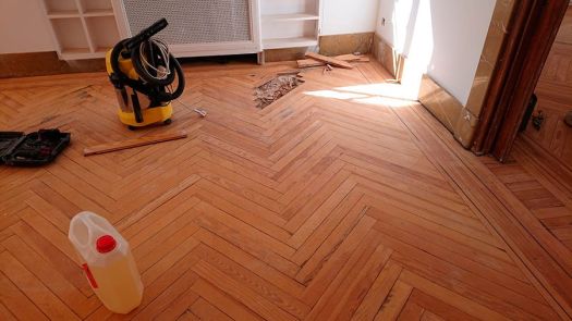 Proceso de reparación y colocación de parquet de madera en espiga, con herramientas y materiales en el suelo de una vivienda