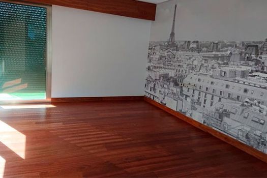 Habitación con suelo de parquet de tono rojizo recién restaurado, pared decorada con mural de París.